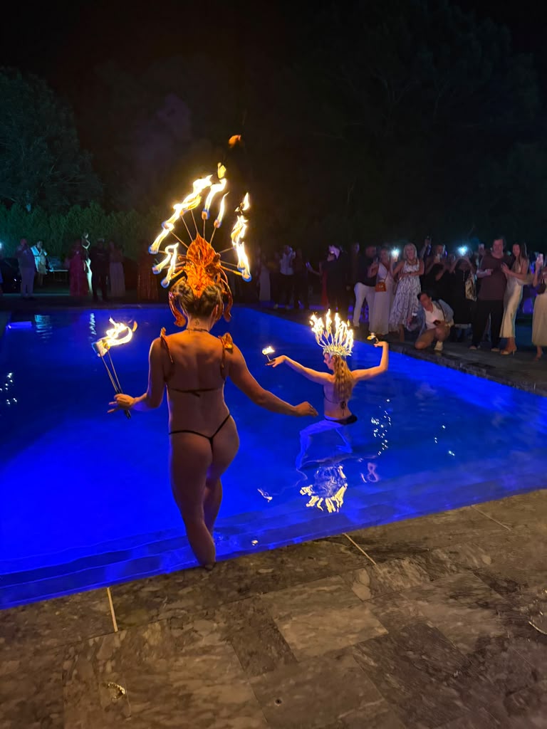 Fire performers wearing flaming headdresses dance in the illuminated pool at The Art Affair