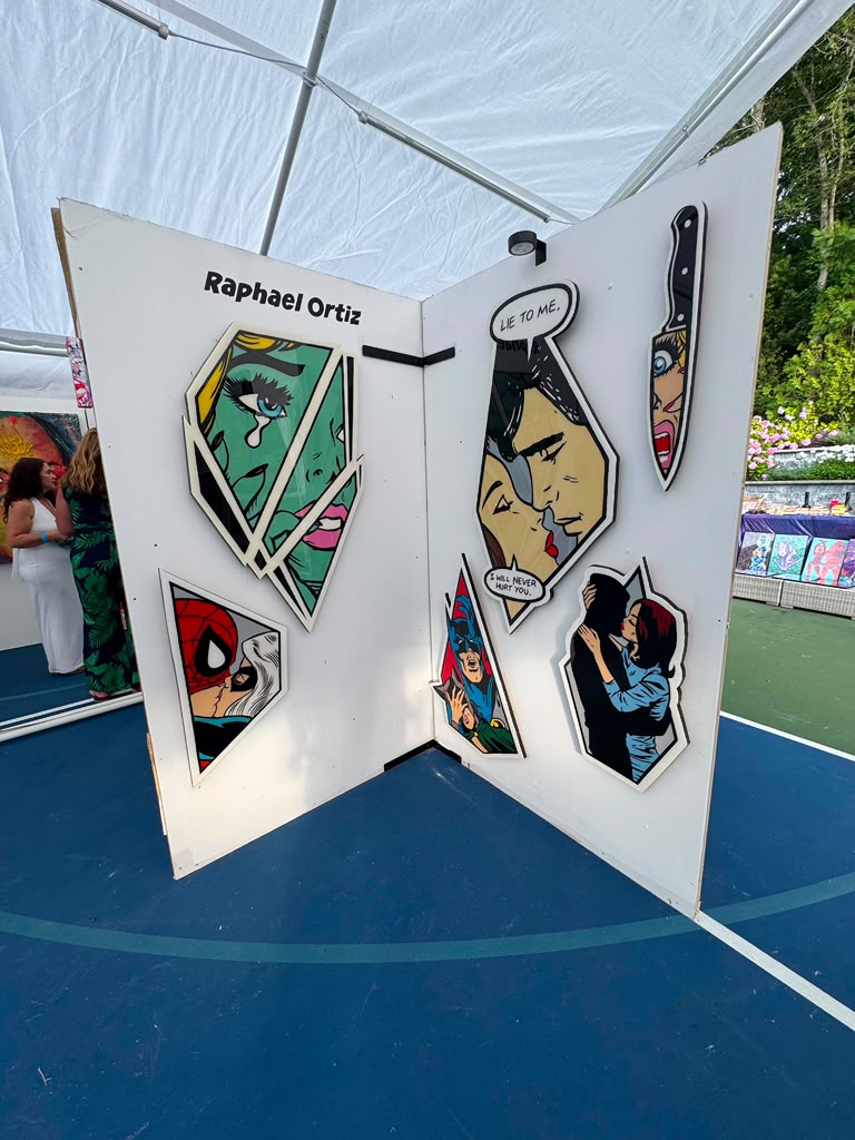 Pop-art comic-style artwork by Raphael Ortiz on display under a tent at The Art Affair