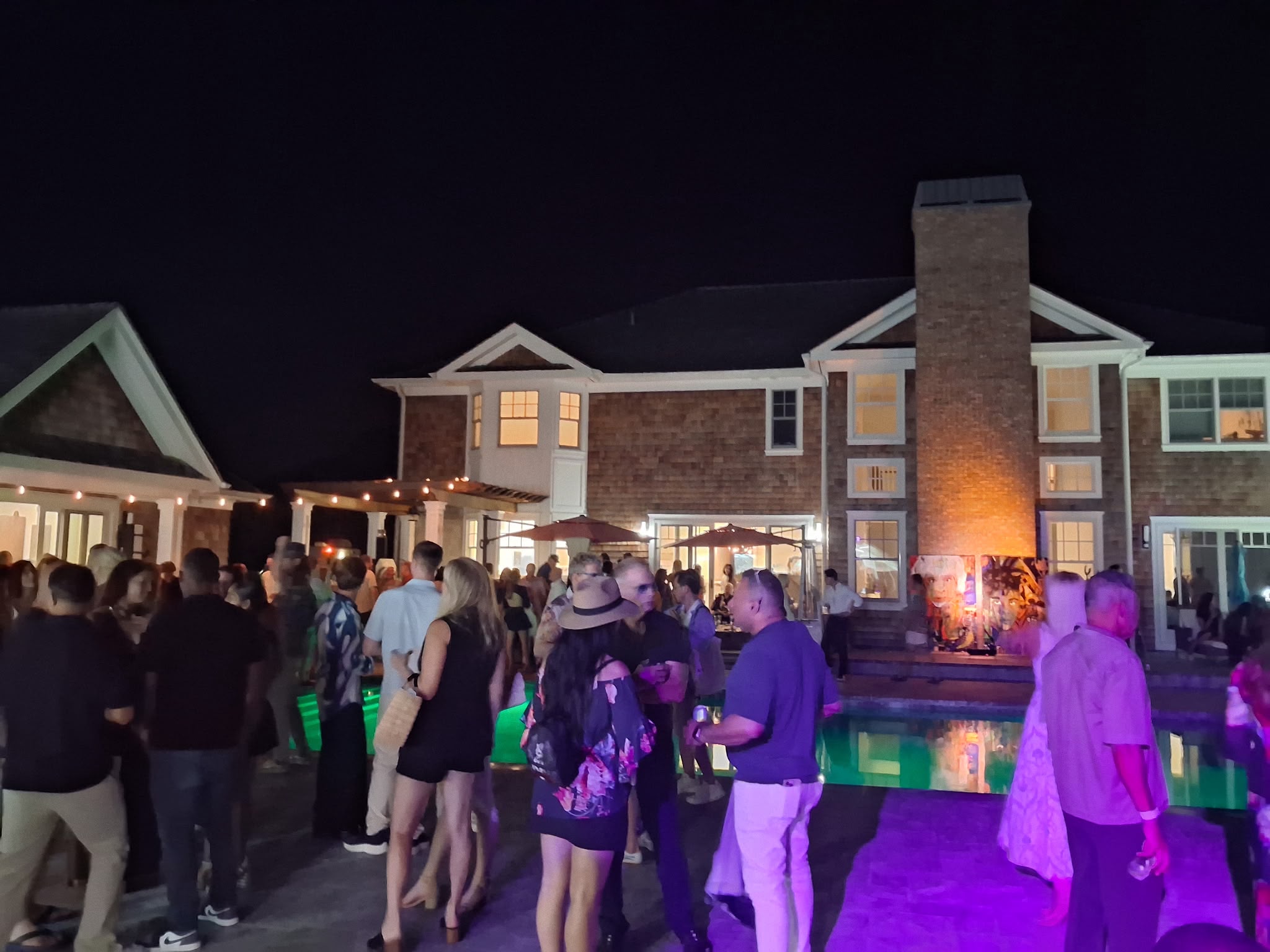 Guests mingle poolside at the Southampton estate hosting The Art Affair at night