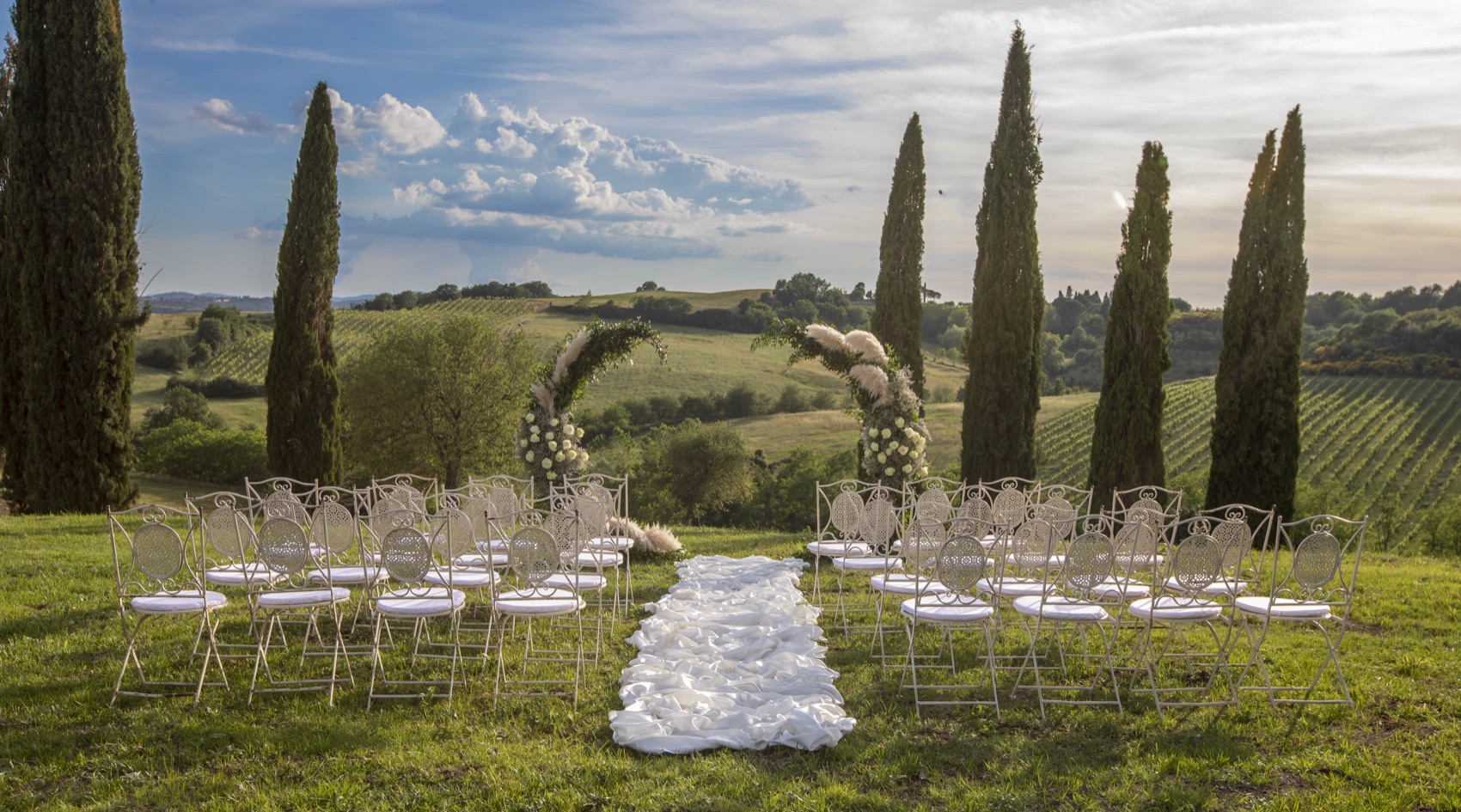 White ceremony aisle framed by cypress trees over the Tuscan vineyards